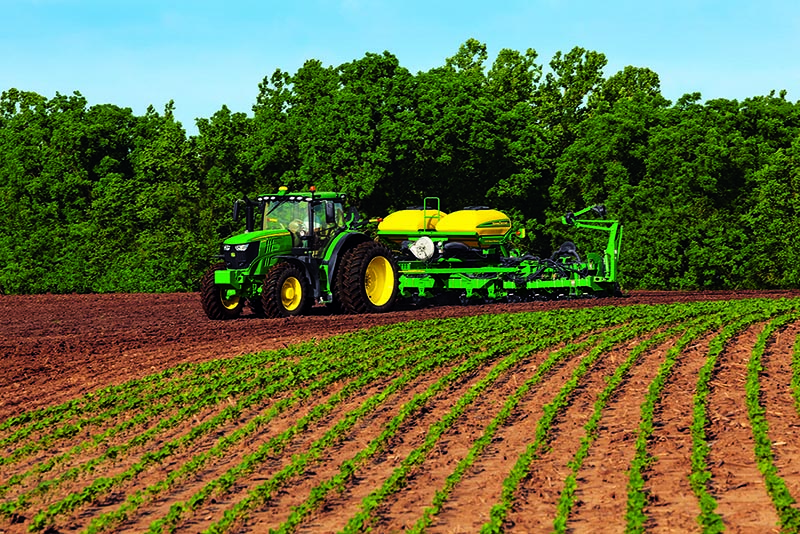 A John Deere tractor pulling a sprayer in a field of soybeans