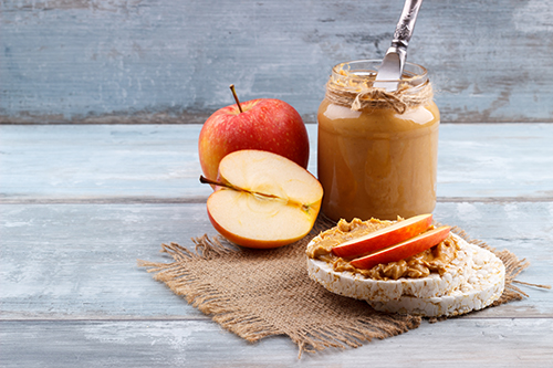 A jar of peanut butter with apples sitting on a table