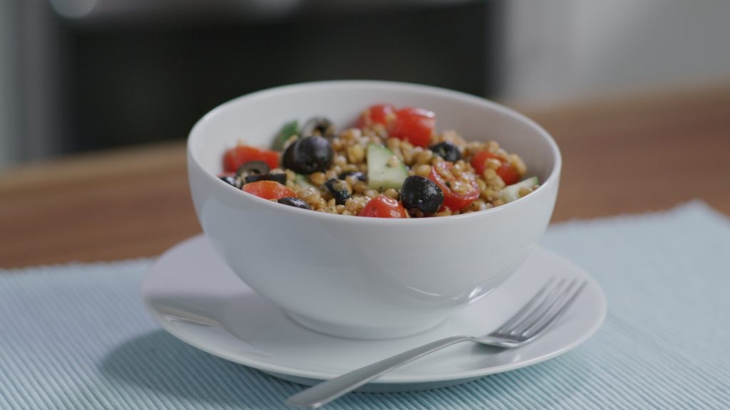 A bowl of wheat berry and lentil salad, sitting on a table.