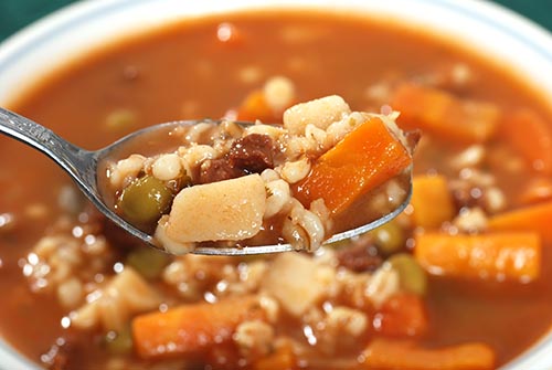 A close up of a spoonful of beef and barley soup