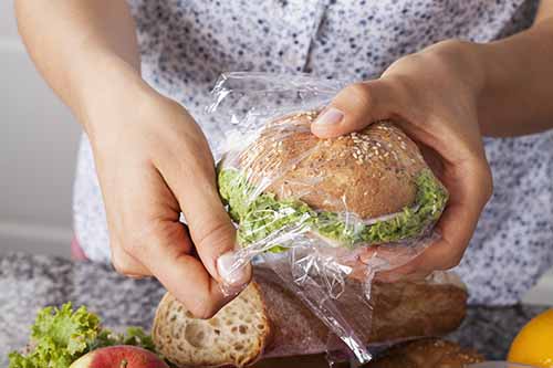 A sandwich in a plastic bag being unwrapped by hands