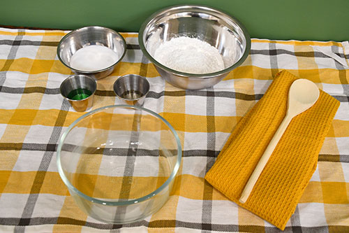 Bowls filled with ingredients for Corn Slime recipe on a white and yellow plaid background