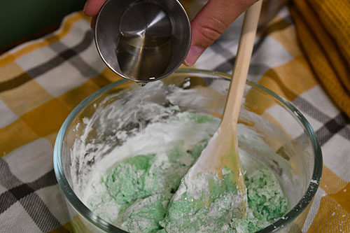 Pouring corn based cooking oil into slime mixture. Stirring with a wooden spoon in a clear glass container