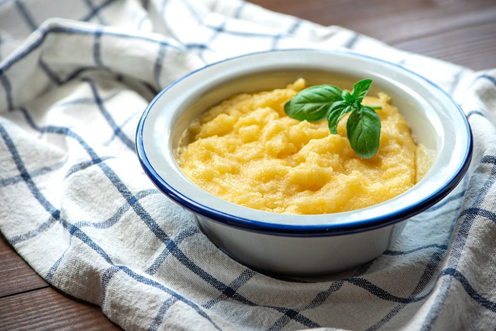 Basic polenta in a bowl on wooden background. Traditional Italian food, vegan food.