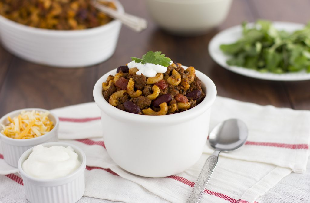 bowl of chili macaroni using beans, beef and grains garnished with cheese and sour cream.