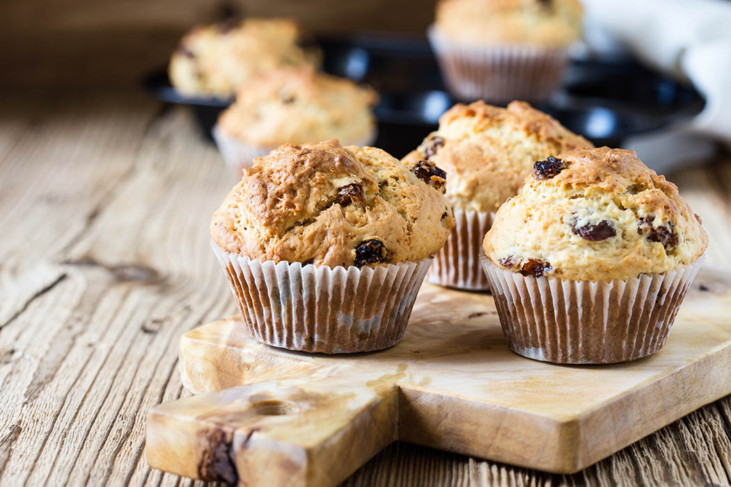 breakfast cornmeal muffins with raisins on a wood serving platter on a wood table.