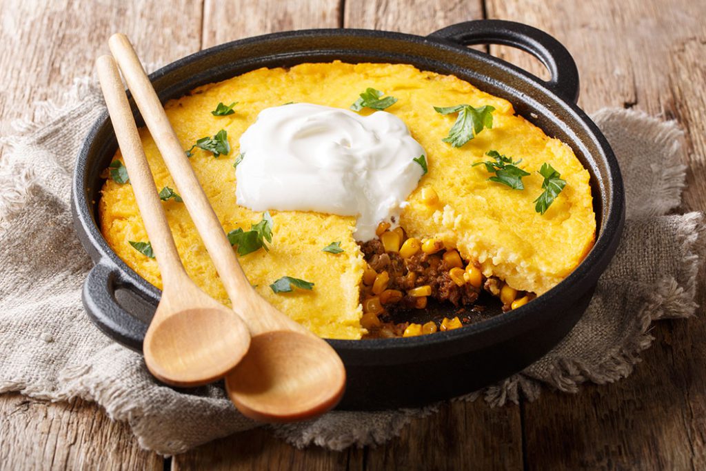 Tamale pie casserole served with sour cream close-up in a pan on the table.