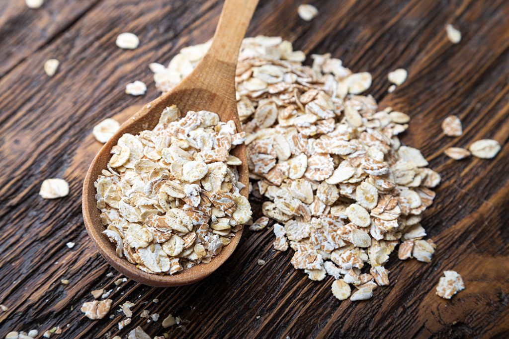 raw oatmeal flakes on wood spoon on wooden table