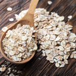raw oatmeal flakes on wood spoon on wooden table
