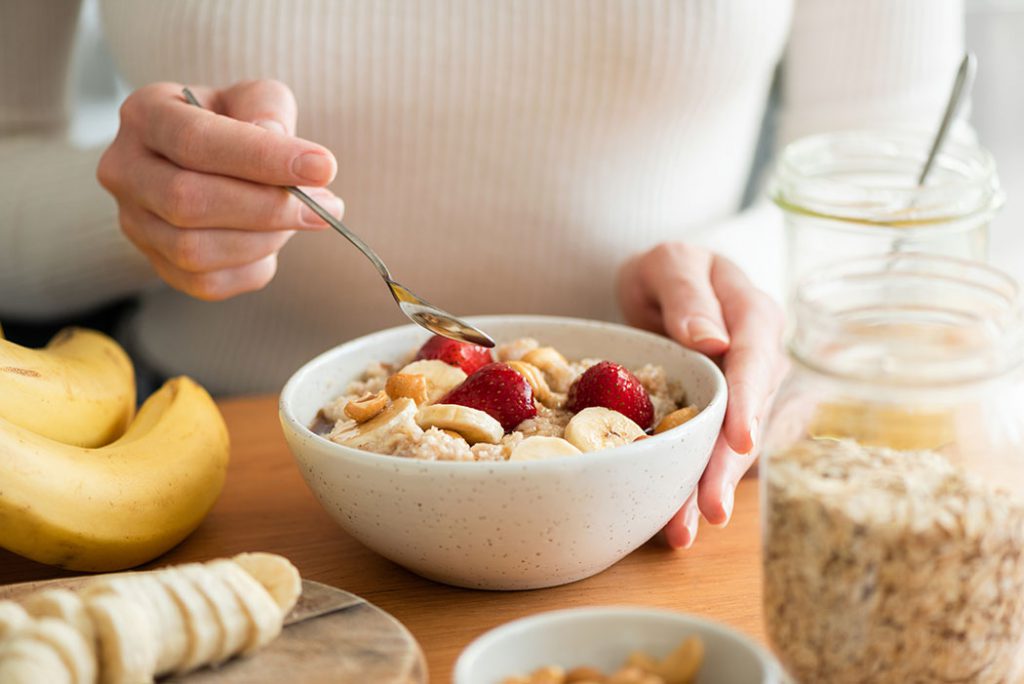 Bowl of oatmeal topped with chopped bananas, strawberries, and nuts. 