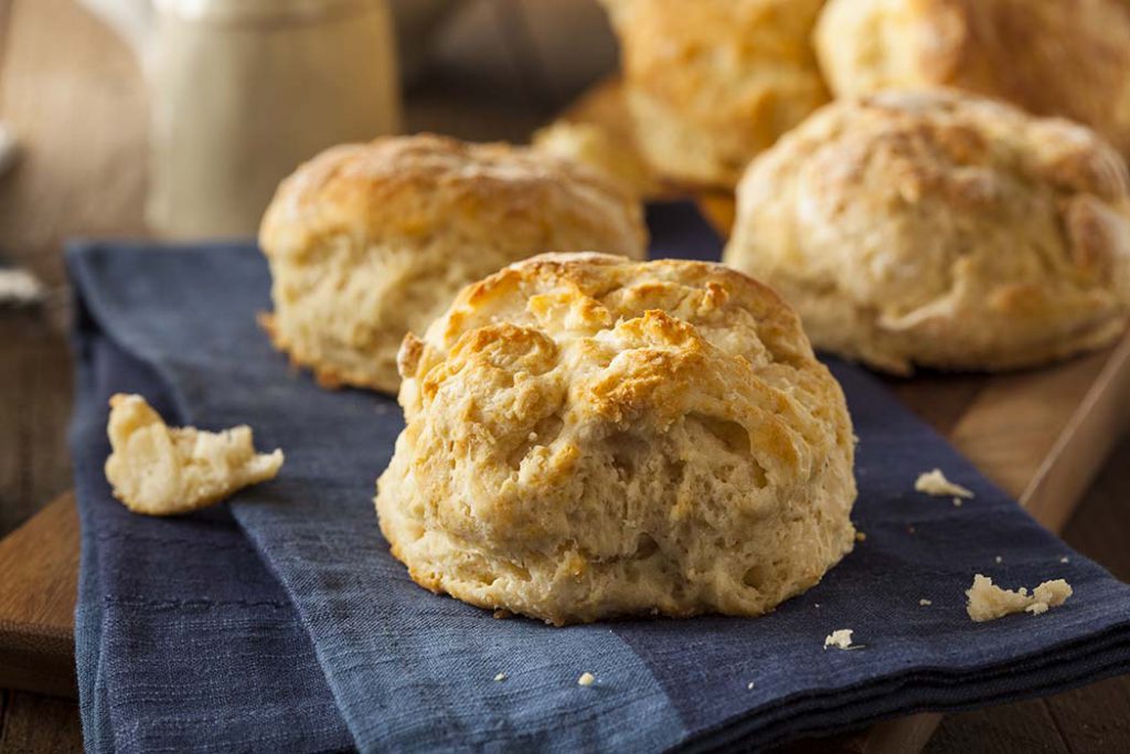 Homemade flakey biscuits on a navy tablecloth on a wood table.