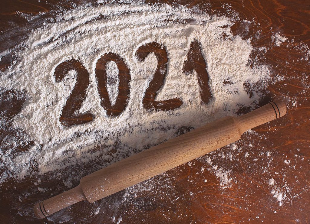 2021 written on white flour on a wooden table with a rolling pin.