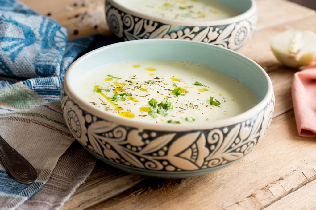 Bowl of creamy oat milk and whole grain oat soup with fresh vegetables. 