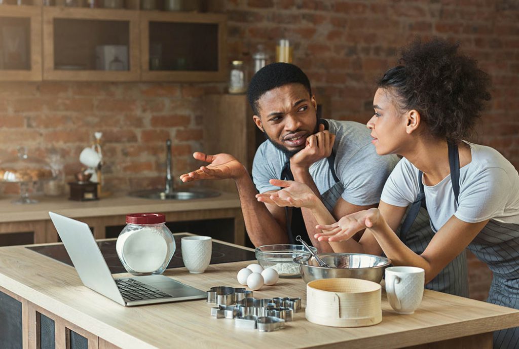 Confused black couple cooking pastry with recipe on laptop