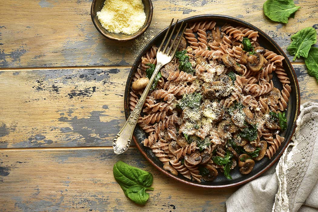 Whole wheat fusilli pasta with mushroom and spinach on a dark plate over old rustic wooden background.Top view with copy space.