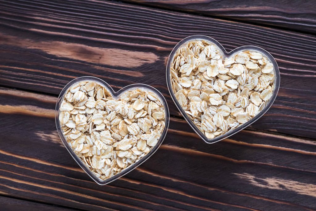 Raw oat-flakes on dark wood board background. Dry uncooked cereal in two bowl at heart shaped