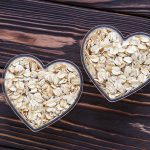 Raw oat-flakes on dark wood board background. Dry uncooked cereal in two bowl at heart shaped