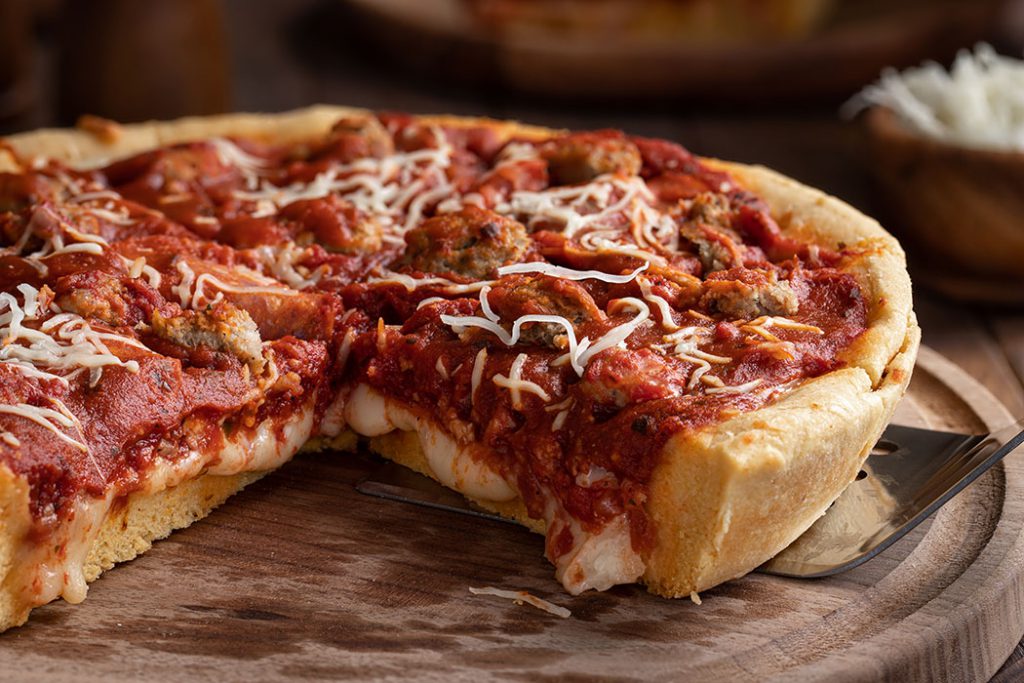 Closeup of a deep dish sausage pizza on a wooden platter