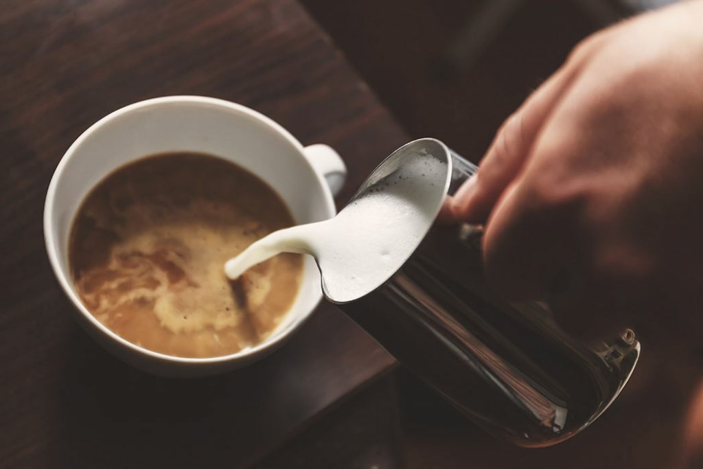 man pouring into a cup of coffee with milk.
