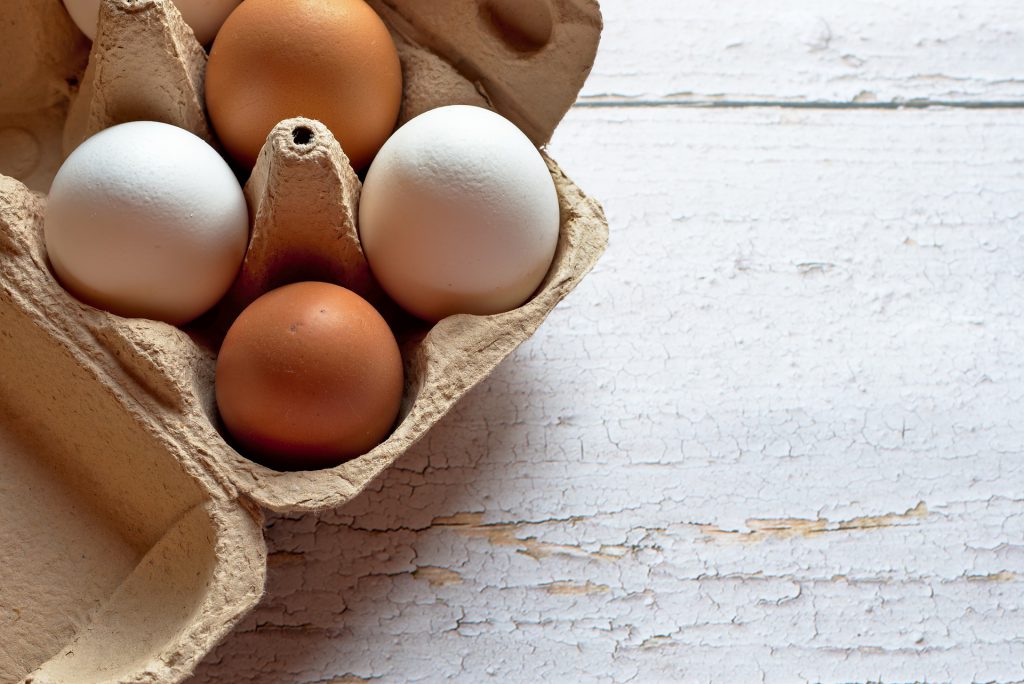 white and brown eggs in an egg carton on a white wooden table. 