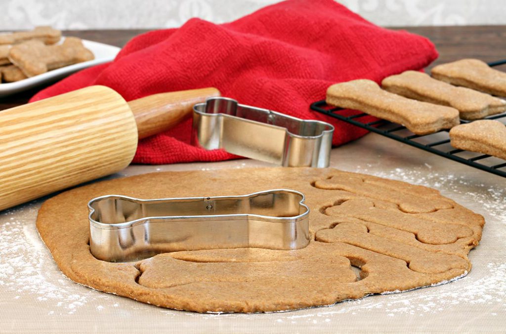 Dog biscuit dough with rolling pin and bone shaped cookie cutters on a silicone mat.